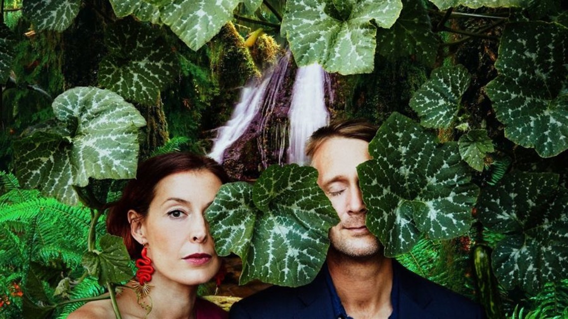 Photo of woman and man behind large green leaves