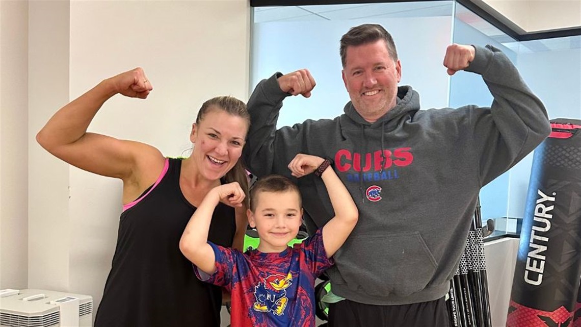 smiling mom, dad and son making strong arms pose in fitness studio