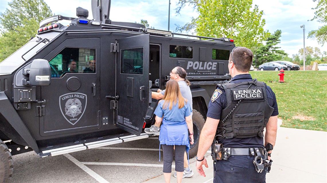 police officer watches man and woman tour tactical vehicle