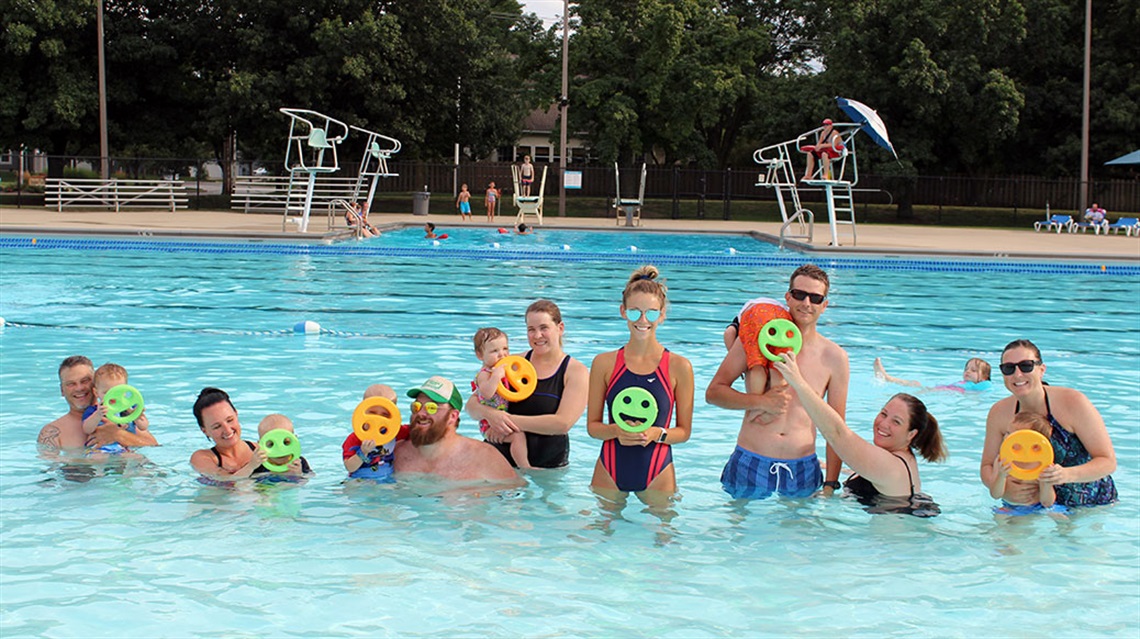 lifeguard and group of people in pool holding smiley faces