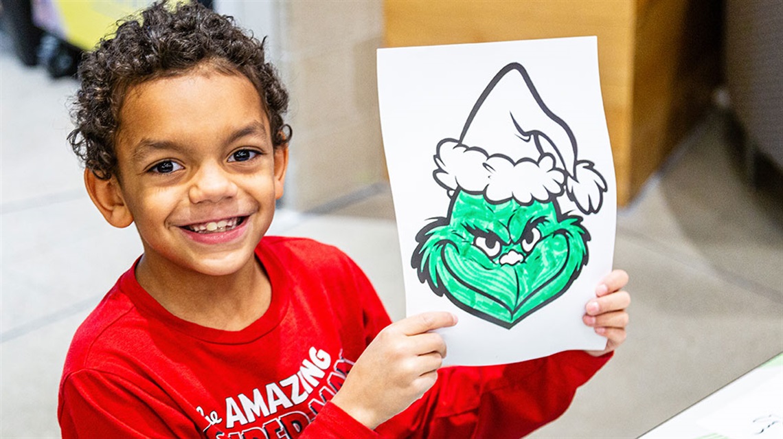 smiling boy shows off The Grinch coloring sheet