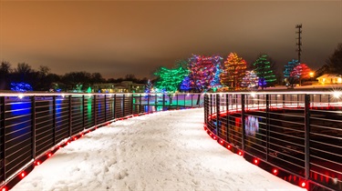 Pond walkway decorated with holiday lights on snowy evening