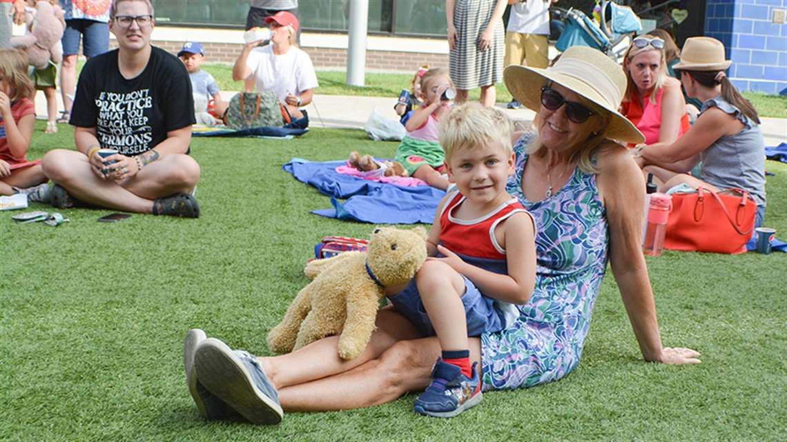 smiling boy with teddy bear sitting on lap of woman