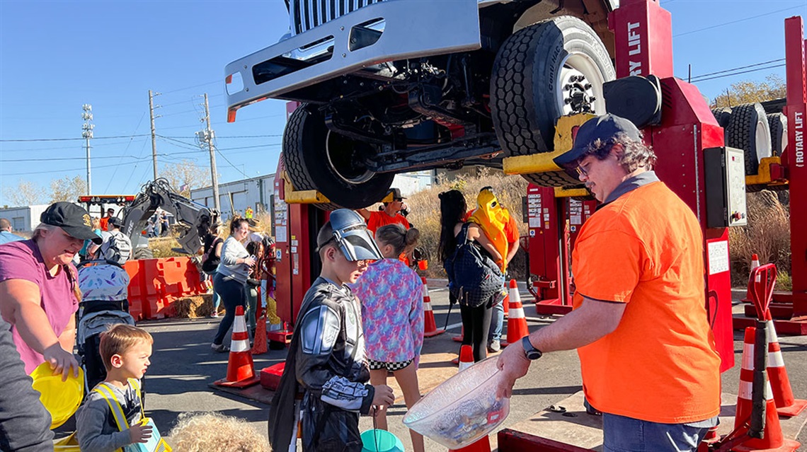 kids pick candy from a bucket while a large truck is suspended overhead in background