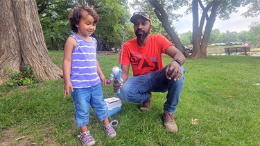Man holds fishing pole while squatting next to young girl