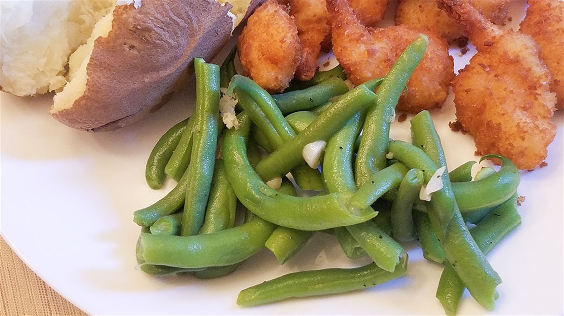 closeup of green beans, potato and chicken on a white plate