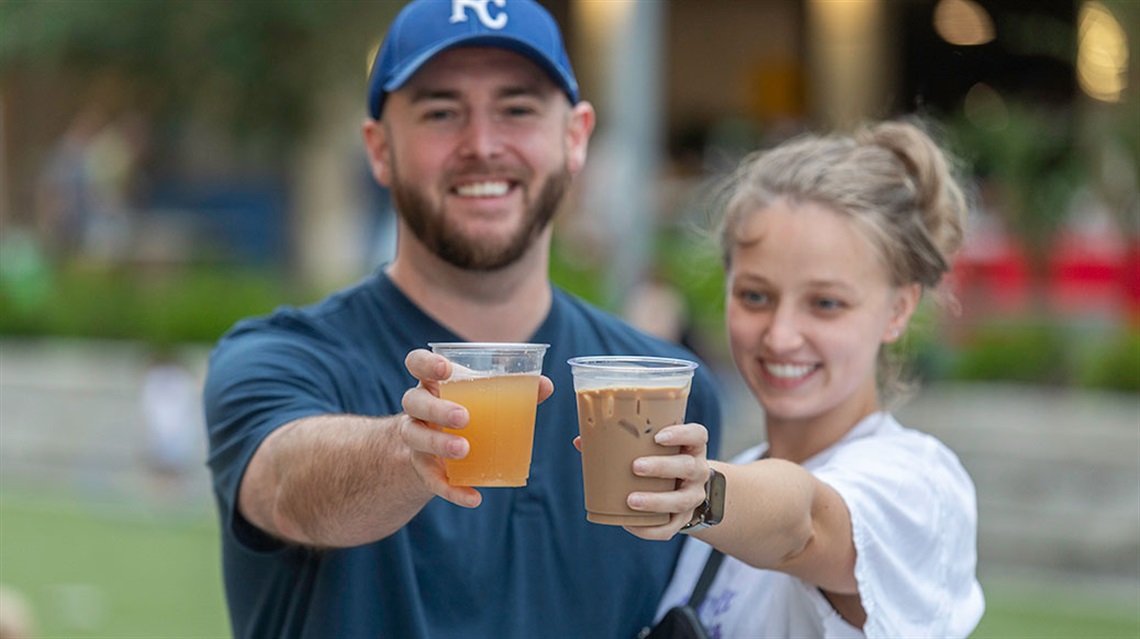 smiling man and women hold out cups of kombucha and ice coffee