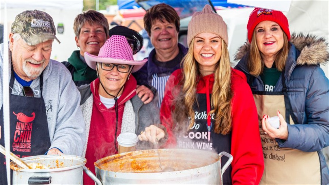 group of people in coats serving chili from a large pot