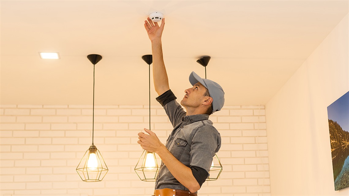 Man in hat checking smoke alarm in ceiling of kitchen