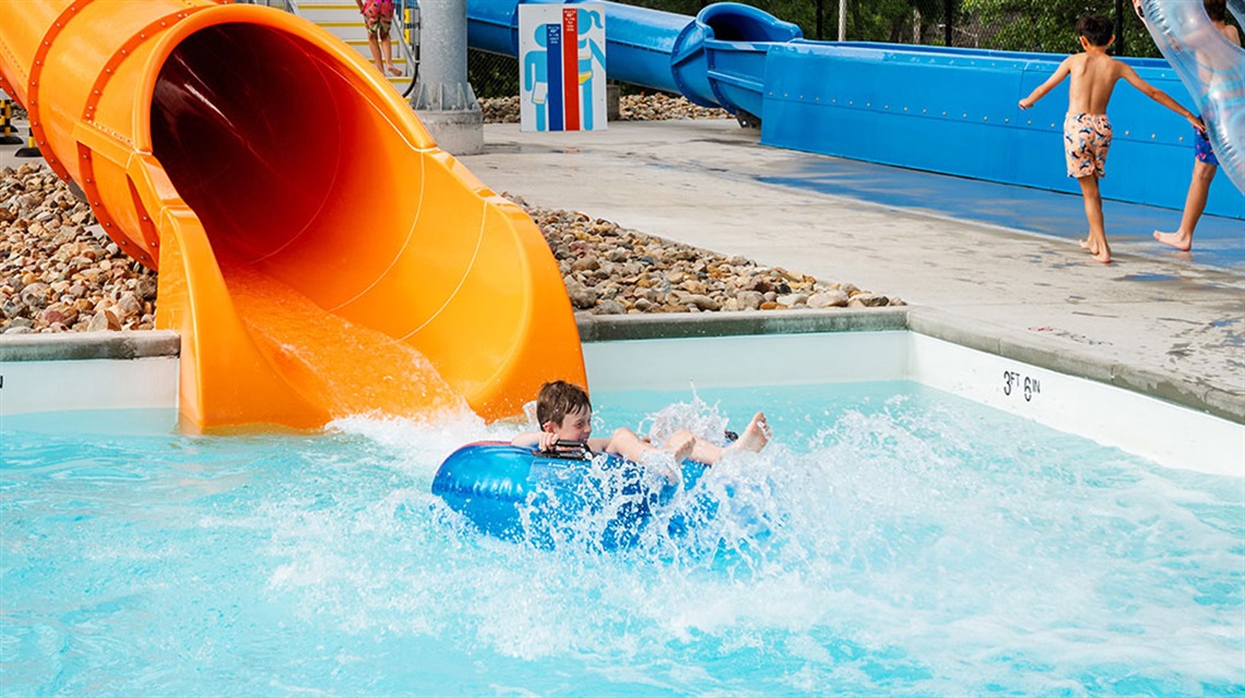 Kid in inflatable tube shooting out from water slide into pool