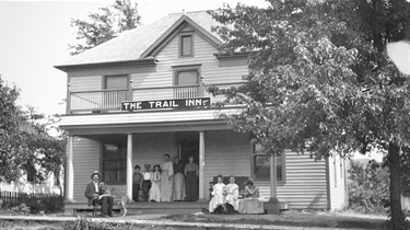 Exterior of The Trail Inn with people posing on porch and in yard