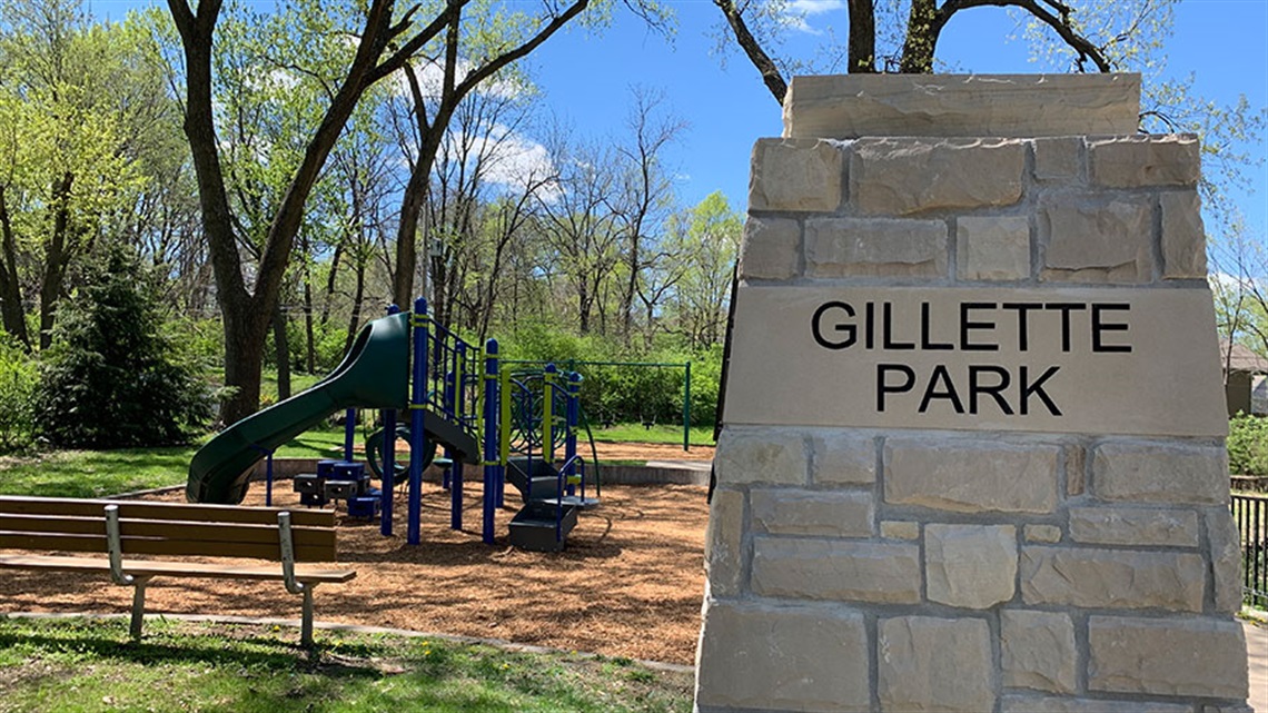 Entrance sign with playground equipment and bench in back