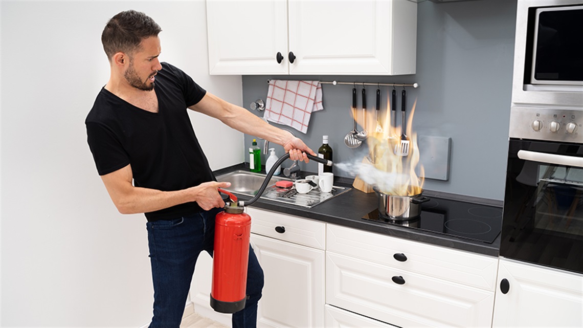 Man putting out kitchen fire with extinguisher