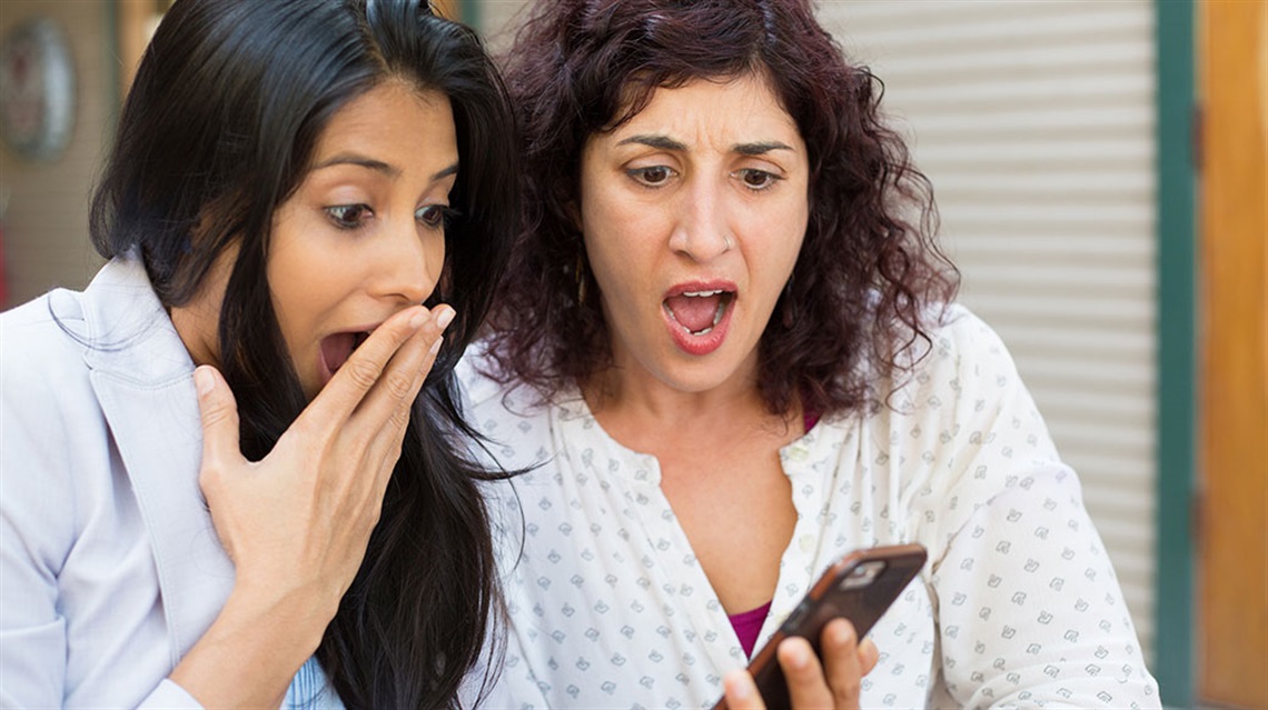 Two women look at cell phone with shocked expressions on their faces