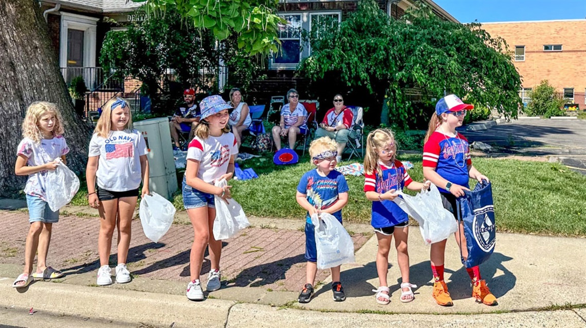 six kids in patriotic apparel standing on a street curb waiting for candy during parade